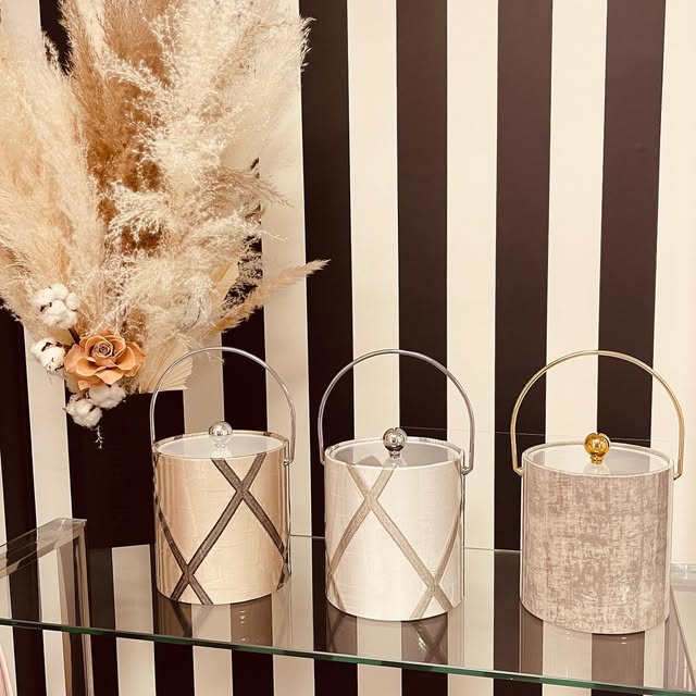 Three neutral ice buckets displayed beneath striped wallpaper